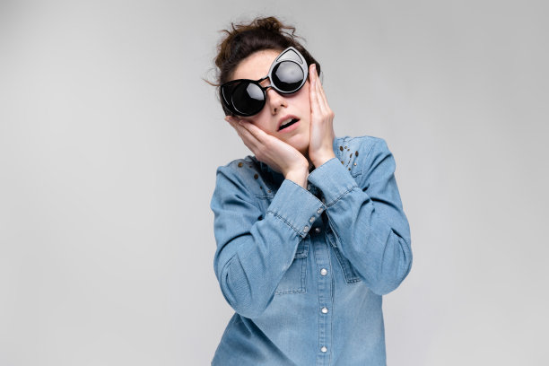 年轻的黑发女孩戴着黑眼镜。猫的眼镜。头发扎成一个髻。这女孩捂着脸。图片下载