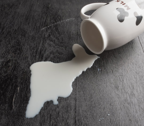 牛奶从玻璃杯里洒在深色的木头上图片下载