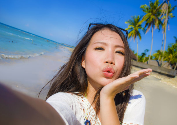 华丽的美丽和快乐的亚洲韩国或中国女性20岁自拍照片发送亲吻与手机相机在异国情调的热带海滩享受暑假旅行图片下载