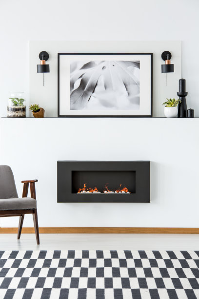 灰色扶手椅在现代客厅的壁炉旁边，配有海报和地毯。真实的照片图片下载