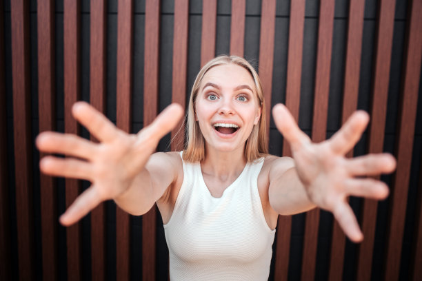 快乐和快乐的女孩看着镜头，试图用她的手指去够它。她眼睛睁得大大的，同时还在微笑。在条纹背景上隔离图片下载