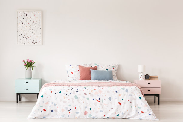 柜子上面的海报，床的旁边有花，白色的卧室里有彩色的枕头。真实的照片图片下载