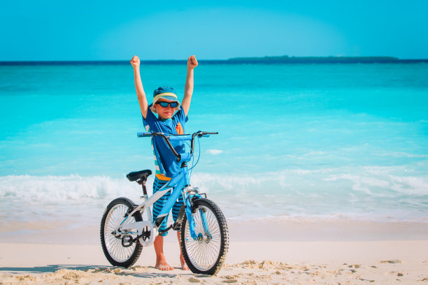快乐的小男孩在热带海滩上骑自行车图片下载