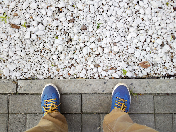 双脚踩在沥青上。脚附近的鹅卵石。白色的小石子。图片下载