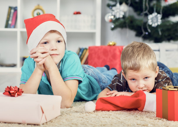 悲伤的男孩戴着圣诞老人的帽子，等待着可以打开礼物的时候。图片下载