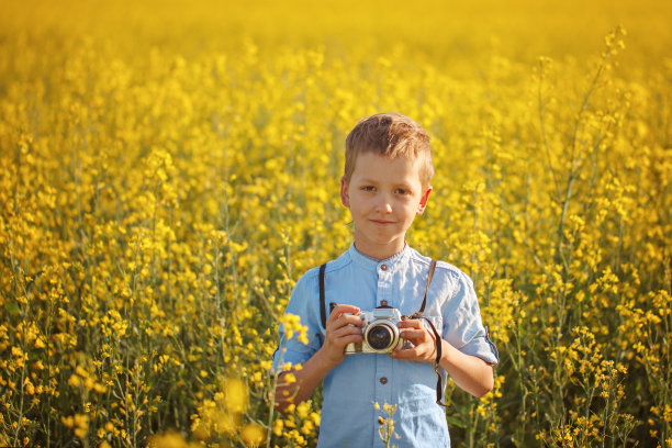 小男孩的肖像摄影师与相机在日落黄色的田野背景图片下载