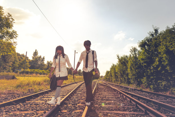 一对穿着校服的亚洲夫妇在铁路上散步图片下载