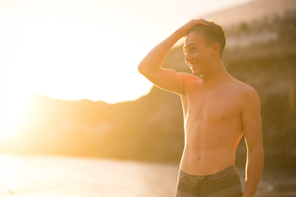 年轻美丽的男孩少年14岁在海滩在美丽的金色日落。微笑，享受户外的自然生活方式。漂亮的身体。图片下载