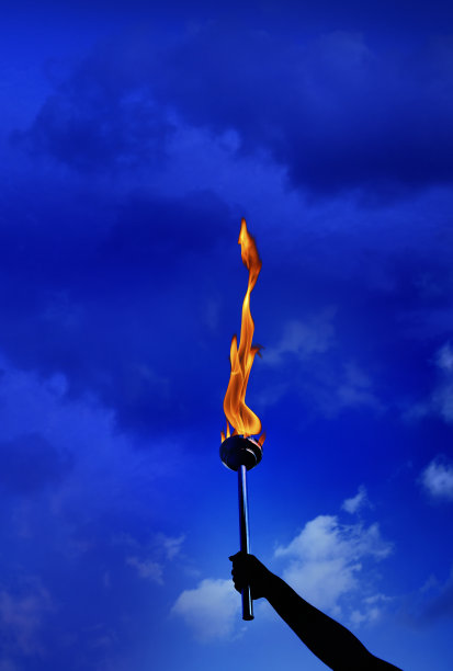 近手握燃烧燃烧的火炬与火焰在多云的蓝色天空图片下载