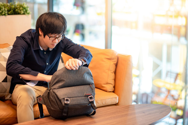一名年轻的亚洲男子坐在客厅的沙发上，把数码平板电脑放进包里图片下载