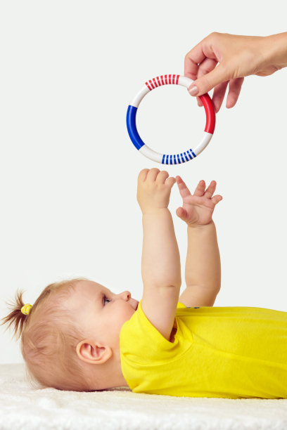 可爱的小女孩试图够到塑料摇铃玩具的工作室肖像图片下载