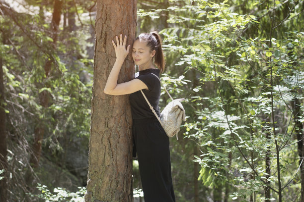 在森林里，背着背包的女孩闭着眼睛拥抱着一棵树。夏天阳光灿烂的日子。图片下载