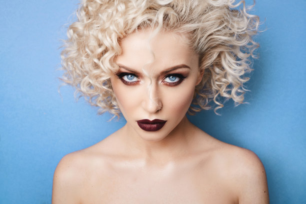 美丽的肖像，时尚和时尚的模特女孩与惊人的蓝色眼睛，卷曲的金发和专业明亮的化妆隔离在工作室的蓝色背景图片下载