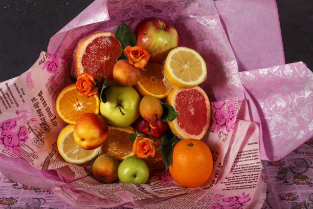 一束新鲜水果与柑橘和玫瑰包裹在彩色包装纸。水果芳香，有新鲜的水果和鲜花。图片下载