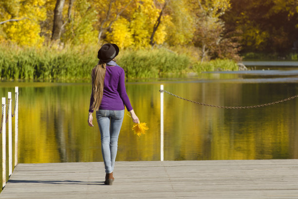 戴帽子的女孩站在码头上。秋天的阳光灿烂的日子。后视图图片下载