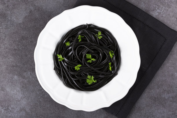 小麦胚芽和黑墨鱼汁意大利面。白色盘子上放黑意大利面和欧芹。宏。前视图。图片下载