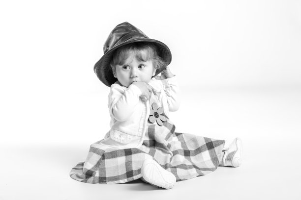 优雅快乐的小女孩1岁，戴着黑色皮帽坐在演播室的地板上。白色背景。幸福的概念。图片下载