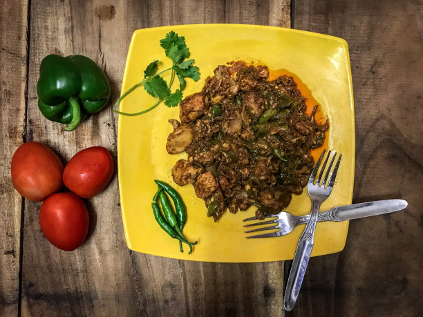 一个纤维盘子，里面有炸鸡和钙，还有西红柿，辣椒和香菜，放在木块上图片下载