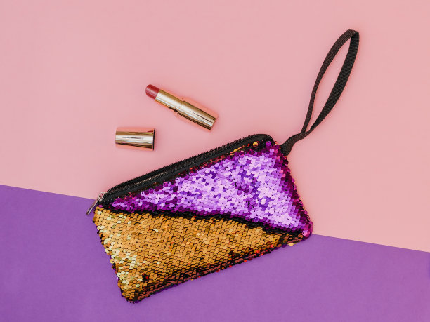 紫色与金色的女士手提包和口红在两色桌子上。柔和的颜色。平的。图片下载