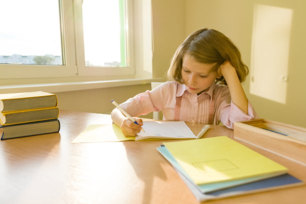 女学生，8岁的女孩，坐在桌子前拿着书，在笔记本上写东西。学校、教育、知识和儿童。图片下载