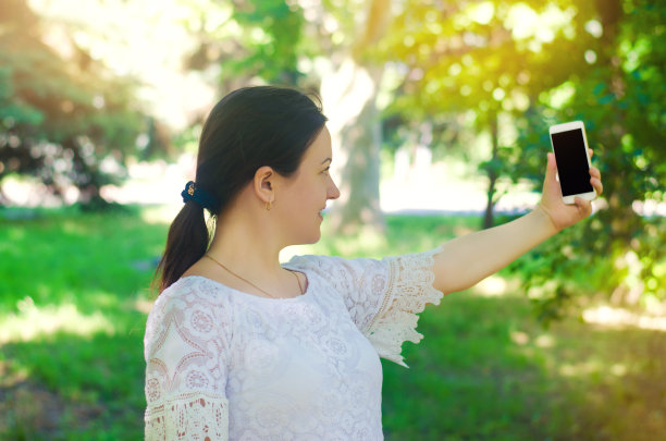 美丽的年轻欧洲女孩褐发拍下自己的照片，并在城市公园自拍。人，生活方式，在新鲜空气中行走。图片下载
