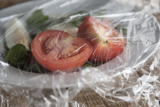 在蔬菜盘上裹一卷塑料薄膜。特写孤立在木制背景上。没有塑料的概念。零怀斯特。图片下载