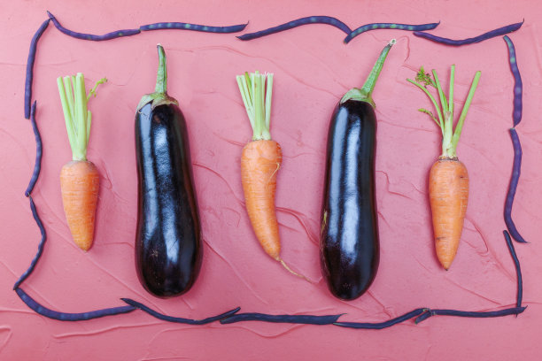 在彩色豆子的框架里，粉红色的背景上是茄子和胡萝卜图片下载
