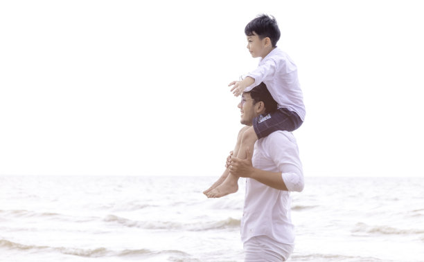 父亲和孩子一起过节。孩子骑脖子父亲照顾在暑假日落和孩子对蓝色的海和天空的背景。假日旅行的概念图片下载