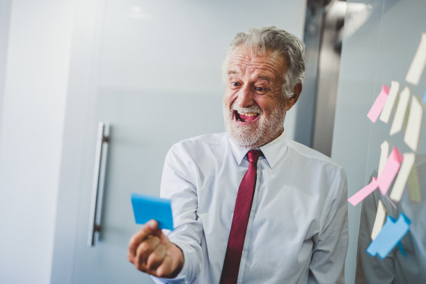 老高级商务人员愉快地工作在办公室，阅读便利贴在房间图片下载