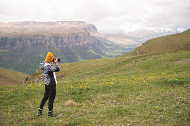一个年轻的女孩在一个阴天的高山顶上拍摄高原的照片。女孩的背影图片下载