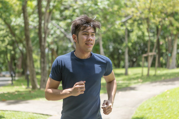 早上在公园里跑步的年轻微笑的运动员。健身的人在公园慢跑。图片下载