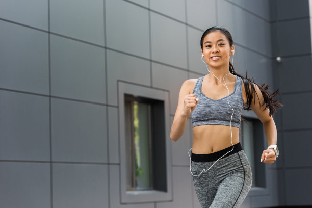 带着耳机微笑的年轻亚洲女运动员在城市街道上奔跑图片下载