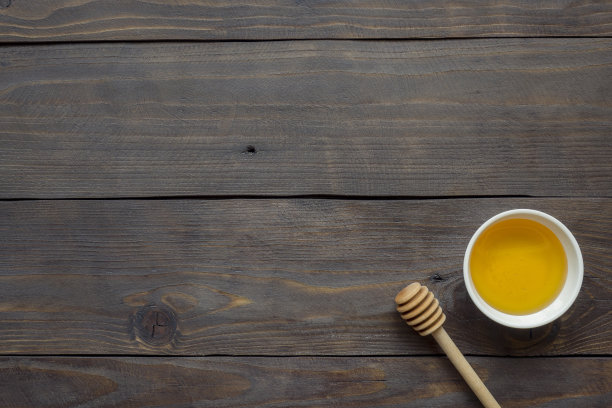 液体蜂蜜在盘子和蜂蜜棒深色木质背景图片下载