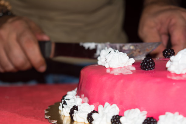 一个粉红色覆盖蛋糕的特写与黑莓和酸奶油在模糊的背景一个男人的手切一份图片下载