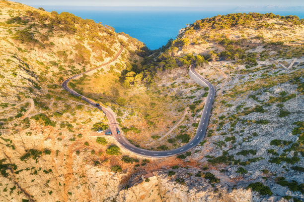 鸟瞰图山路与汽车，绿色森林日落在夏季欧洲。景观有柏油路，树木在岩石上。高速公路穿过公园。俯视图从飞行的无人机。自然图片下载