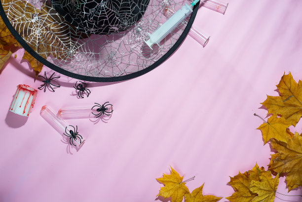 创意万圣节概念照片女巫的帽子，蜘蛛和注射器与深阴影在软粉色的背景图片下载