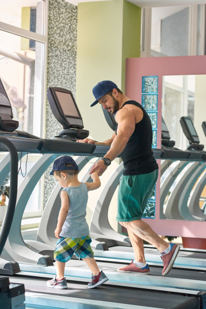 年轻的父亲和小儿子在太空健身房的赛马场上跑步。图片下载