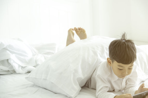 小弟弟躺在卧室的床上玩手机游戏，露出他的脚，看起来很幸福的数字生活和游戏。图片下载