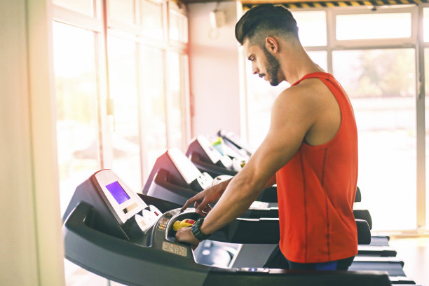 一个年轻人在健身房设置跑步机图片下载