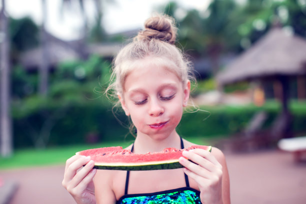 一个女孩在一个非常热的天吃一个冷的西瓜。概念照片的天气炎热，热浪，夏天的季节，孩子，享受生活，快乐，幸福，食物。图片下载