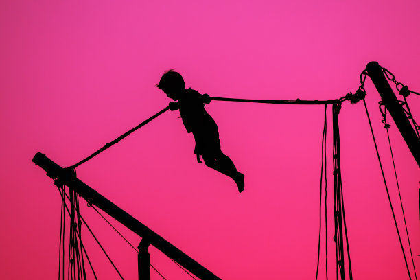 男孩在蹦床上跳的剪影在傍晚红色，粉红色的彩色日落天空背景图片下载