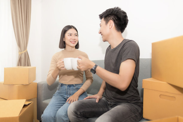 照片的快乐年轻夫妇喝咖啡后打开箱子和搬进新家。图片下载