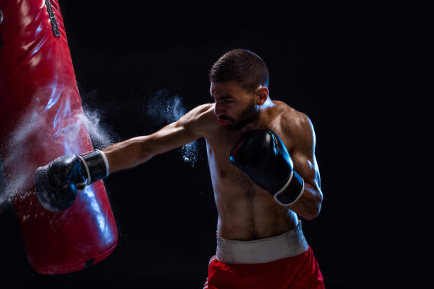 胡子男拳击手训练与沙袋在黑色的背景。男性拳击手作为大搏斗的锻炼图片下载
