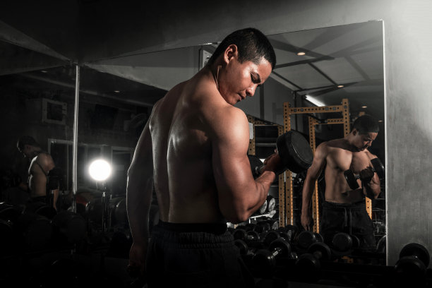 健美运动员在健身房用哑铃锻炼。健美运动员用哑铃锻炼。健身肌肉的身体图片下载