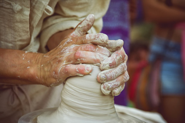 创造一个罐子或花瓶的白色粘土特写。主缸。男人用手制作陶罐。车间里的雕刻家用陶器制作了一个瓦罐。扭曲的陶工旋盘。图片下载