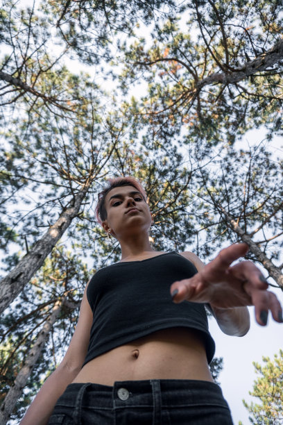 上面的照片与松树树冠的年轻漂亮的朋克女孩在松树森林在日落时间穿着黑布和粉红色的头发图片下载