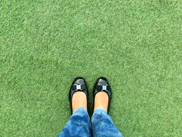 俯视图腿的女人穿着黑色休闲鞋站在绿色的草地上图片下载