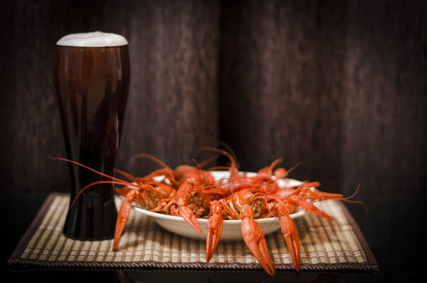 深色背景的桌子上放着一杯啤酒和一盘煮小龙虾图片下载