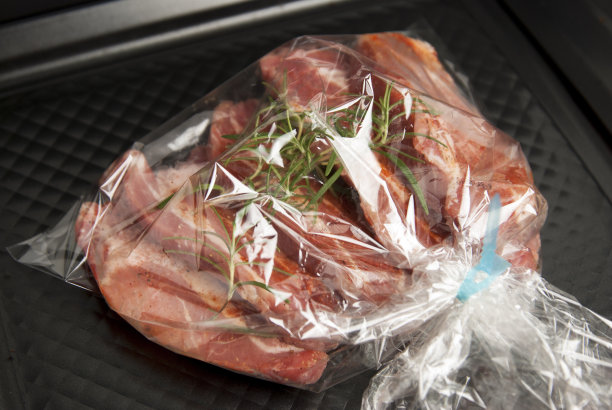 烹饪烘烤塑料袋。没有pastic概念。新鲜的猪肉肉排包装在一个袖子与香料，烘烤准备烘烤，孤立在黑色背景。前视图。图片下载