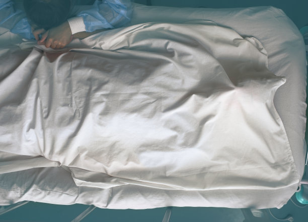 一个年轻的女人在一个被床单覆盖着的死人床边哭泣图片下载